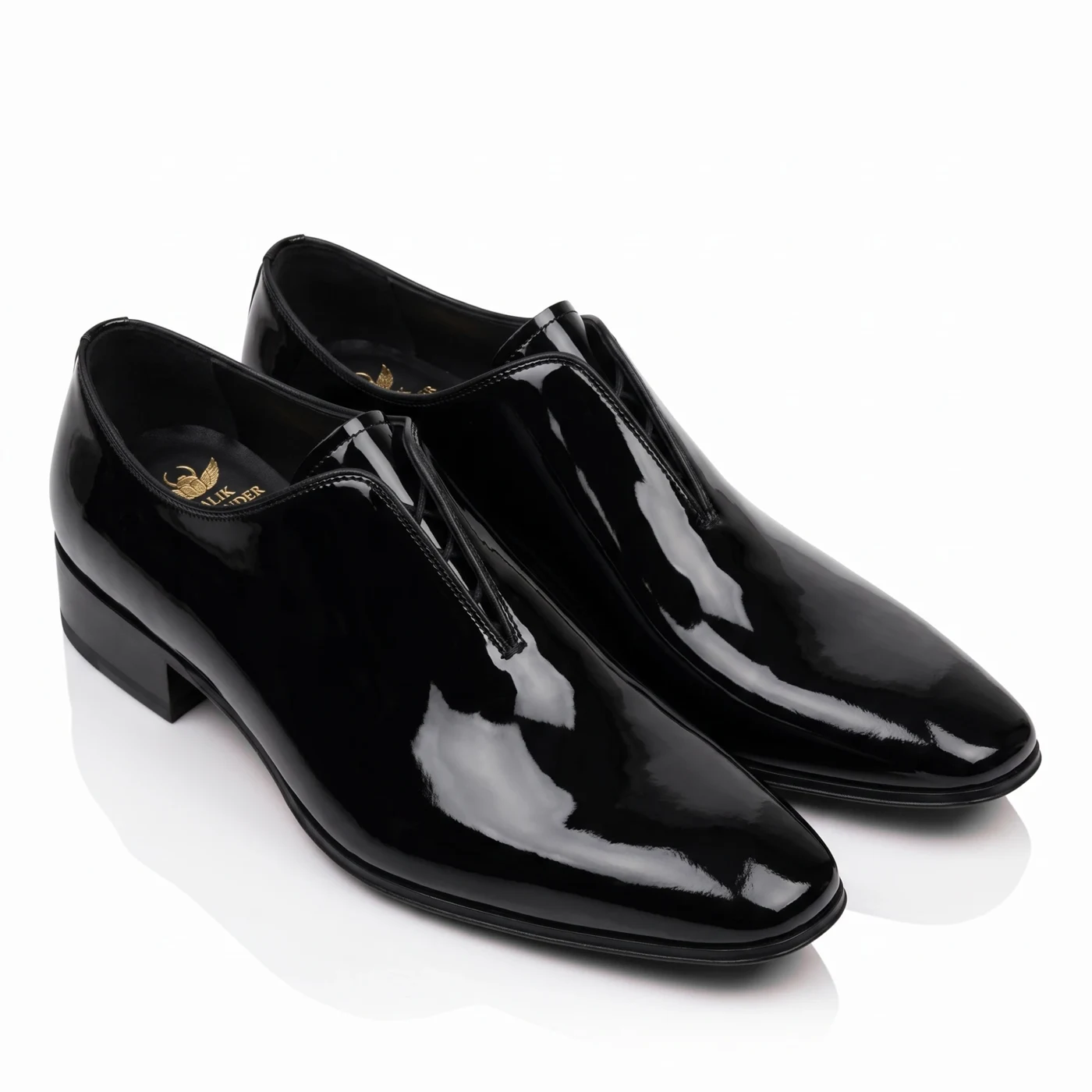 A pair of black patent leather slip-ons from a higher angle, the Malik Alexander logo in gold on the insole